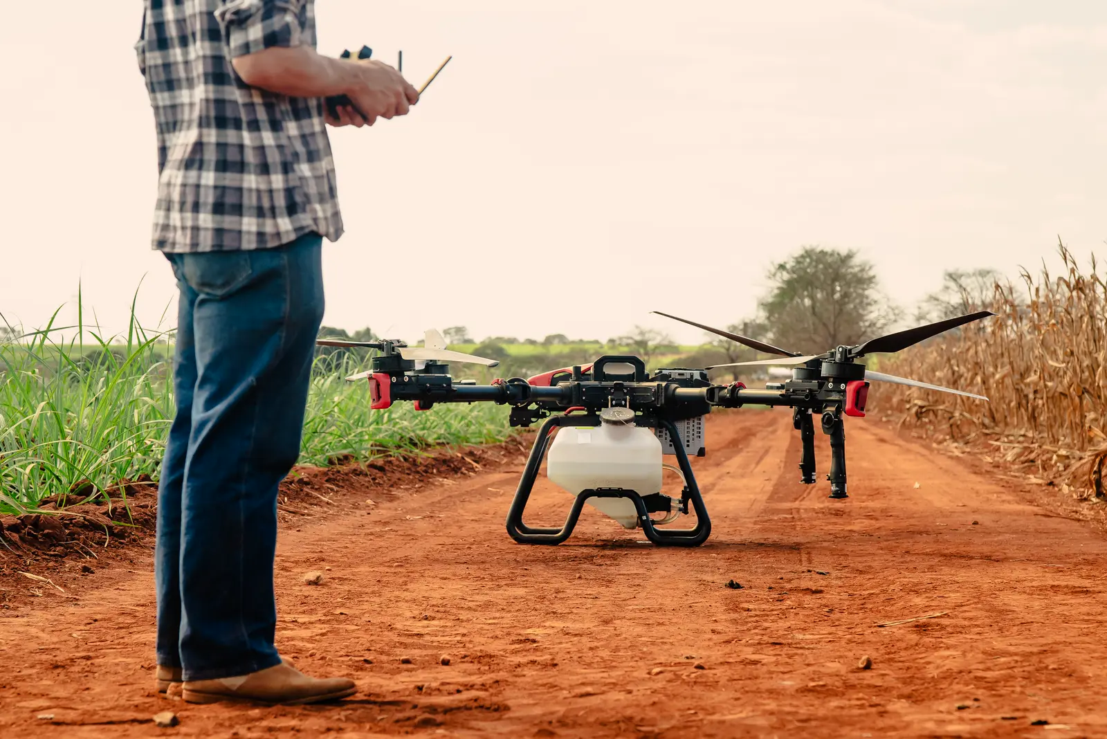 An agricultural spray drone staged on a farm road, its operator readying it for a run.