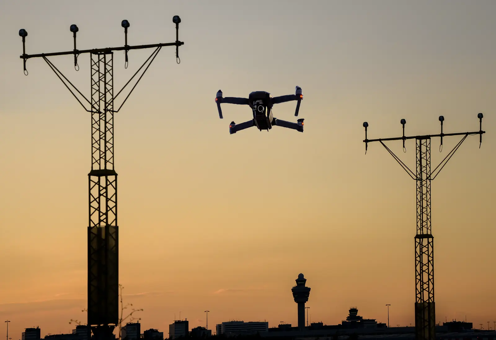 A drone hovering between airfield approach-light masts at sunset.