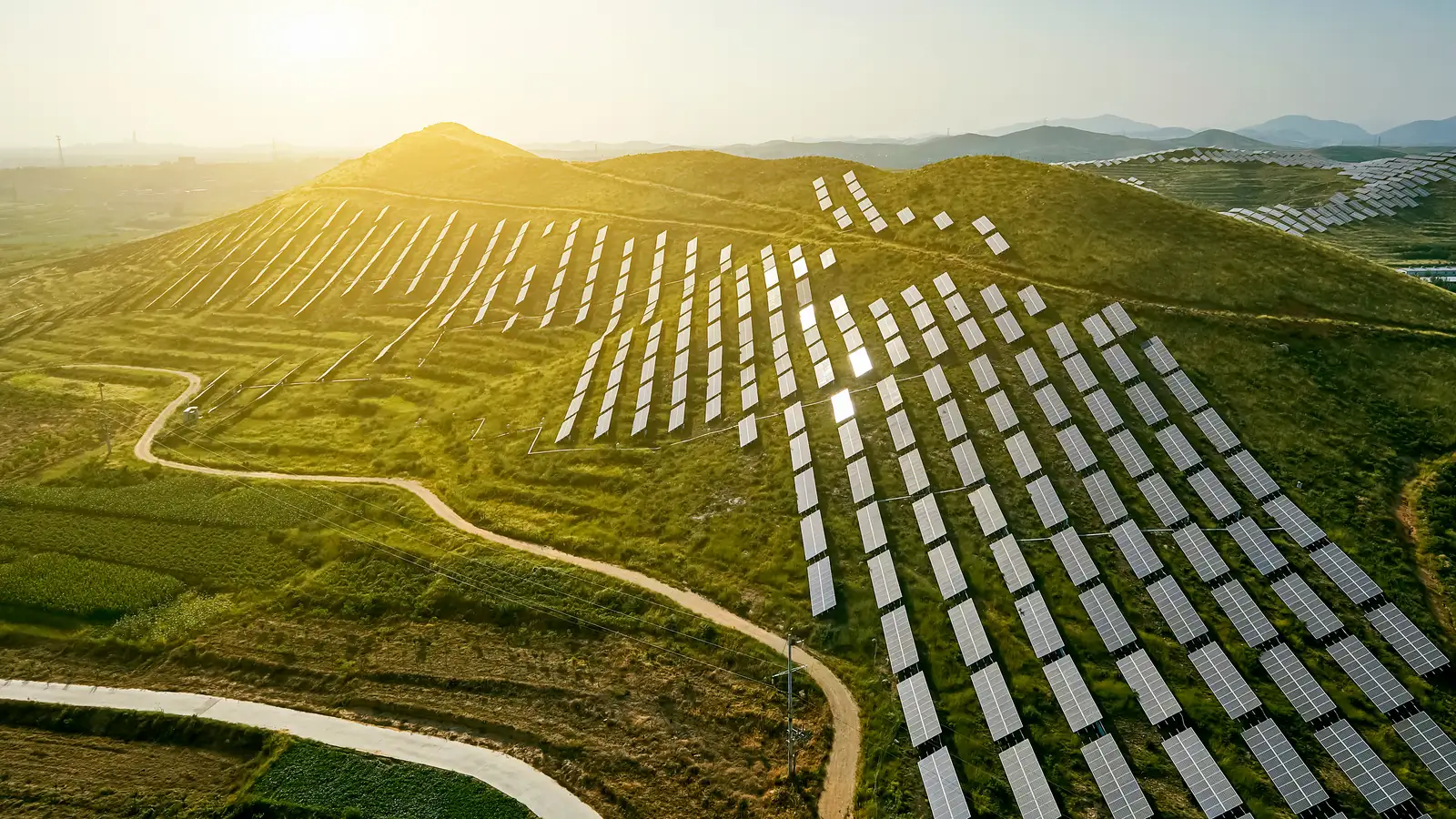 A hillside solar farm at golden hour, panel rows following the terrain.